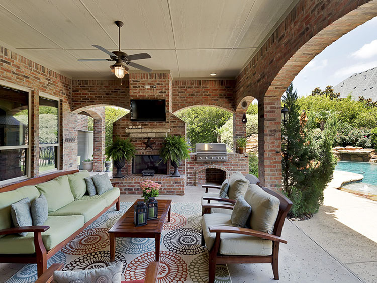 Luxury Patio Ideas - covered patio with brick fireplace and brick arches and columns open to a swimming pool on the right -LifetimeLuxury016